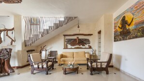 A spacious living room with a high ceiling, a staircase, and a large painting on the wall.