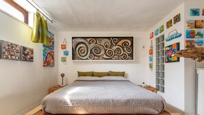 Une chambre à coucher avec un grand lit, une tête de lit en bois, une œuvre d’art accrochée au mur et une fenêtre avec des rideaux.