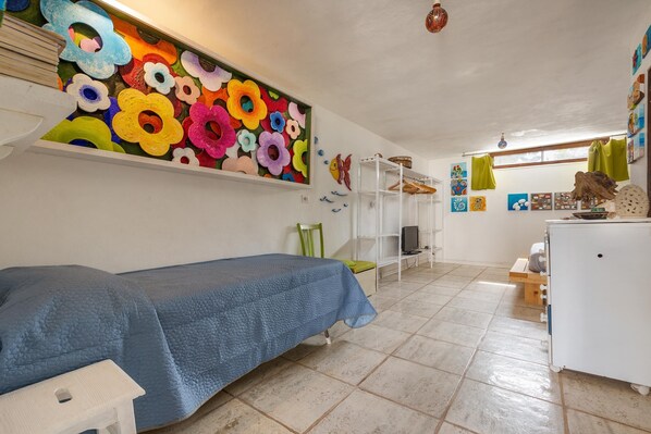 A room with a bed, a colorful flower wall art, a white cabinet, and a shelf with various items.