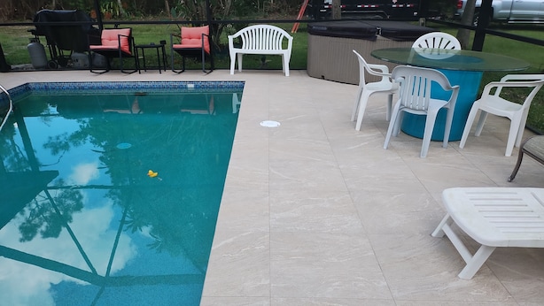 A swimming pool with a tiled deck, surrounded by outdoor furniture including chairs and a table. - Country setting only 10 minutes to  Downtown. (Naples)