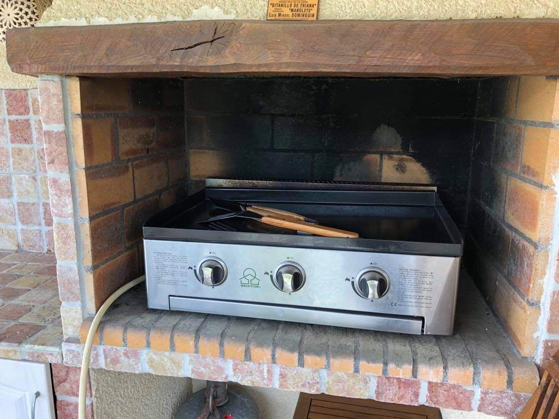 A brick oven grill with a stainless steel cooking surface and three control knobs.