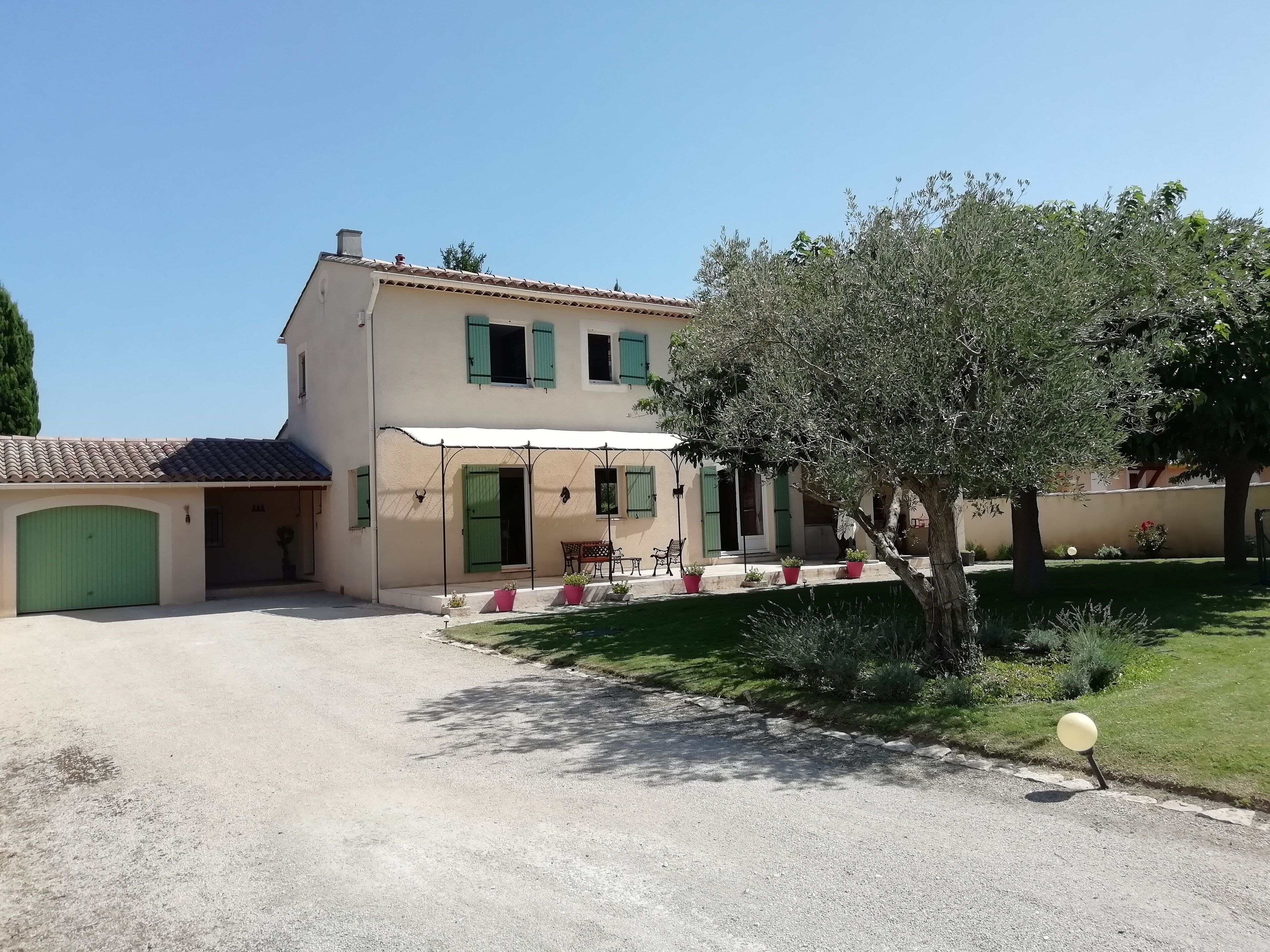 A two-story house with a covered patio, a green garage, and a well-maintained lawn.