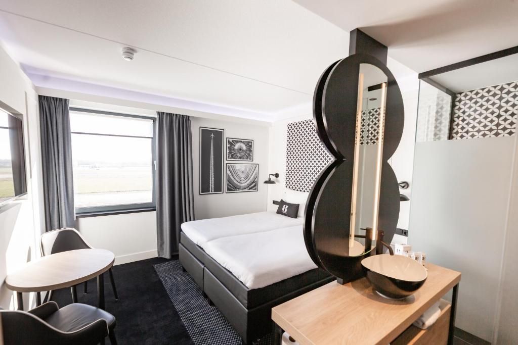 Ein Hotelzimmer mit einem Bett, einem Schreibtisch, einem Sessel, einem großen Spiegel und einem Badezimmer mit Waschbecken und Toilette.
