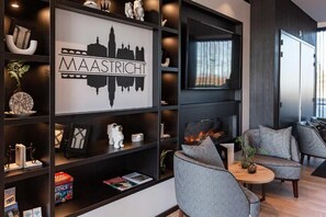 A modern living room with a fireplace, a bookshelf with various decorative items, and a seating area with patterned chairs. - Gr8 Hotel Maastricht-Aachen Airport (Maastricht-Airport)