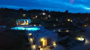 Vue nocturne d’une propriété dotée d’une piscine, de bâtiments en pierre et d’un éclairage extérieur.