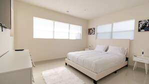 A bedroom with a bed, bedside tables, a TV, and a white dresser.