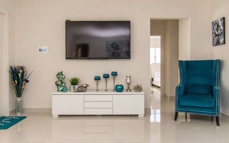 A modern living room with a flat-screen TV mounted on the wall, a white console table with decorative items, and a teal armchair.