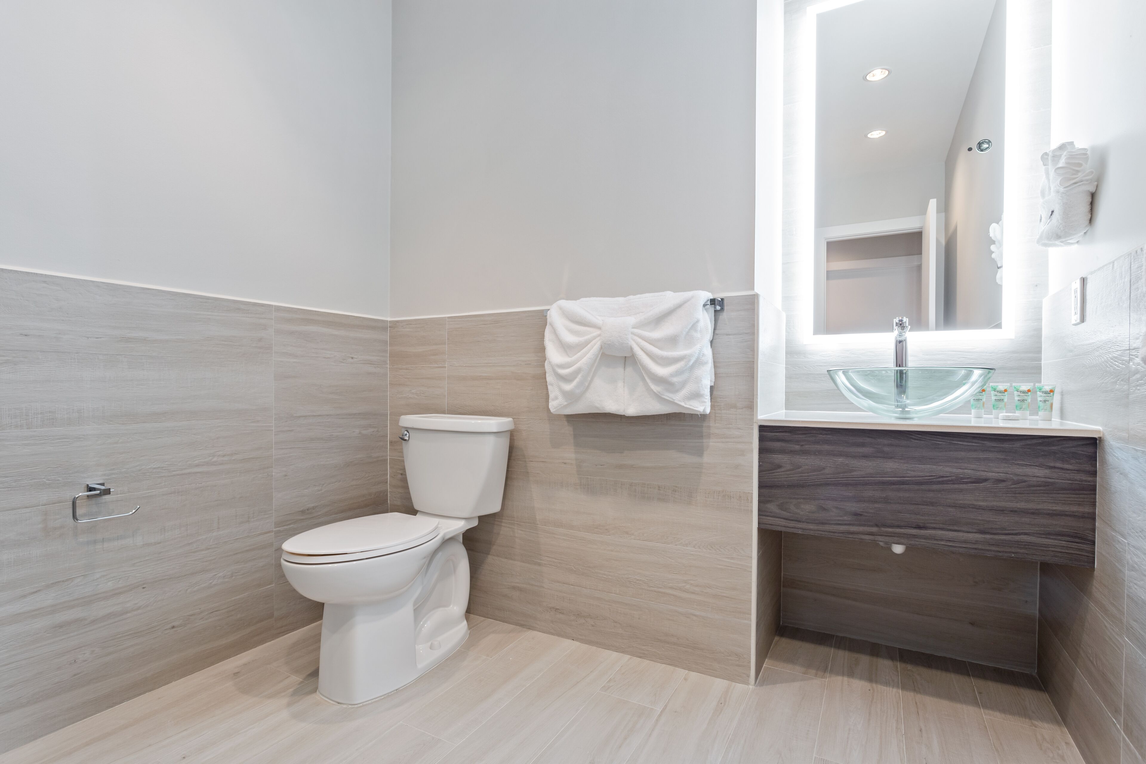 Un baño moderno con inodoro, un lavamanos de vidrio y una toalla colgada en un perchero.