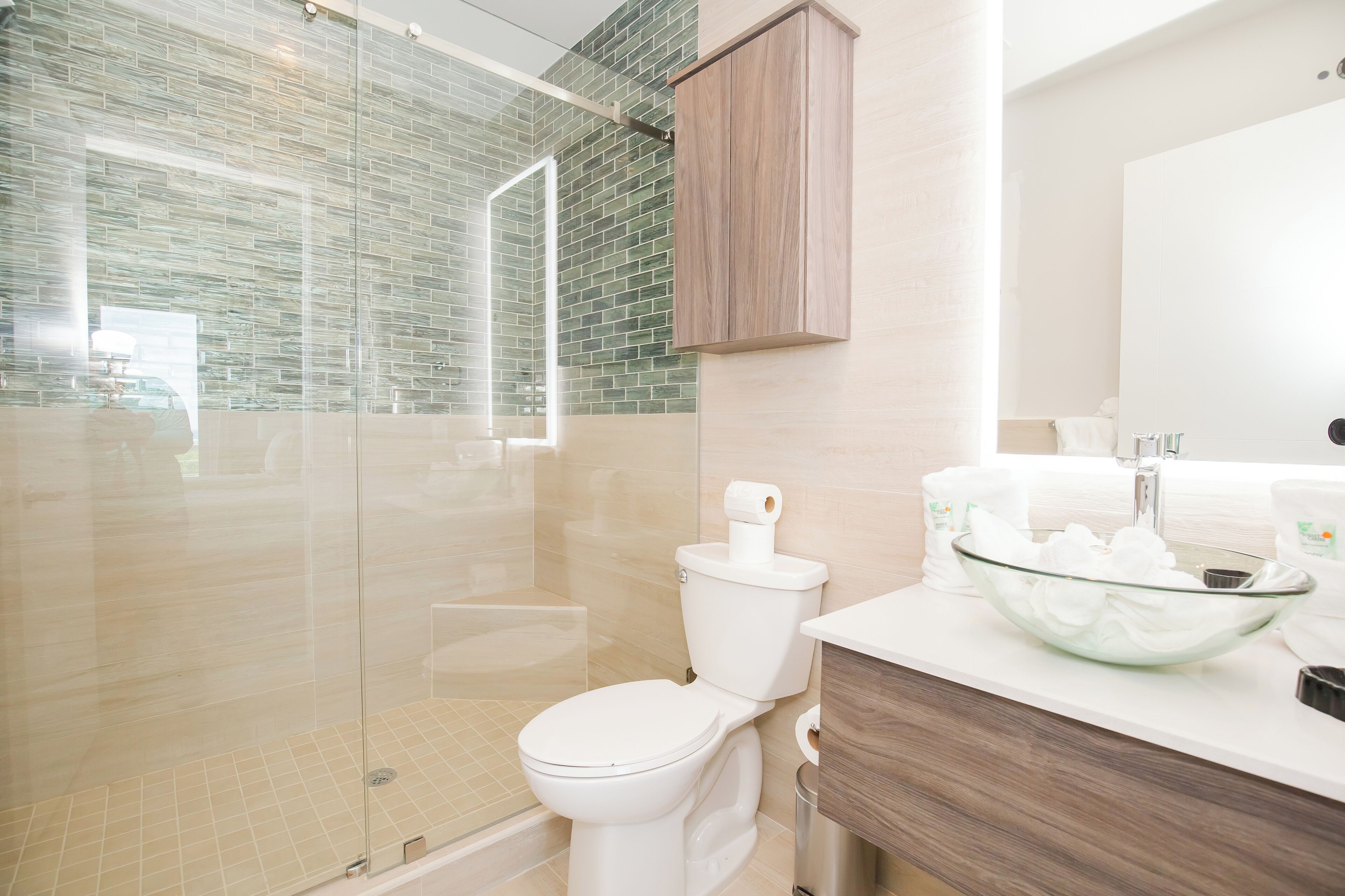 Un baño moderno con ducha envuelta en vidrio, inodoro blanco y lavamanos de vidrio.