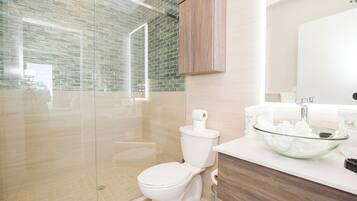 Un baño moderno con ducha envuelta en vidrio, inodoro blanco y lavamanos de vidrio.
