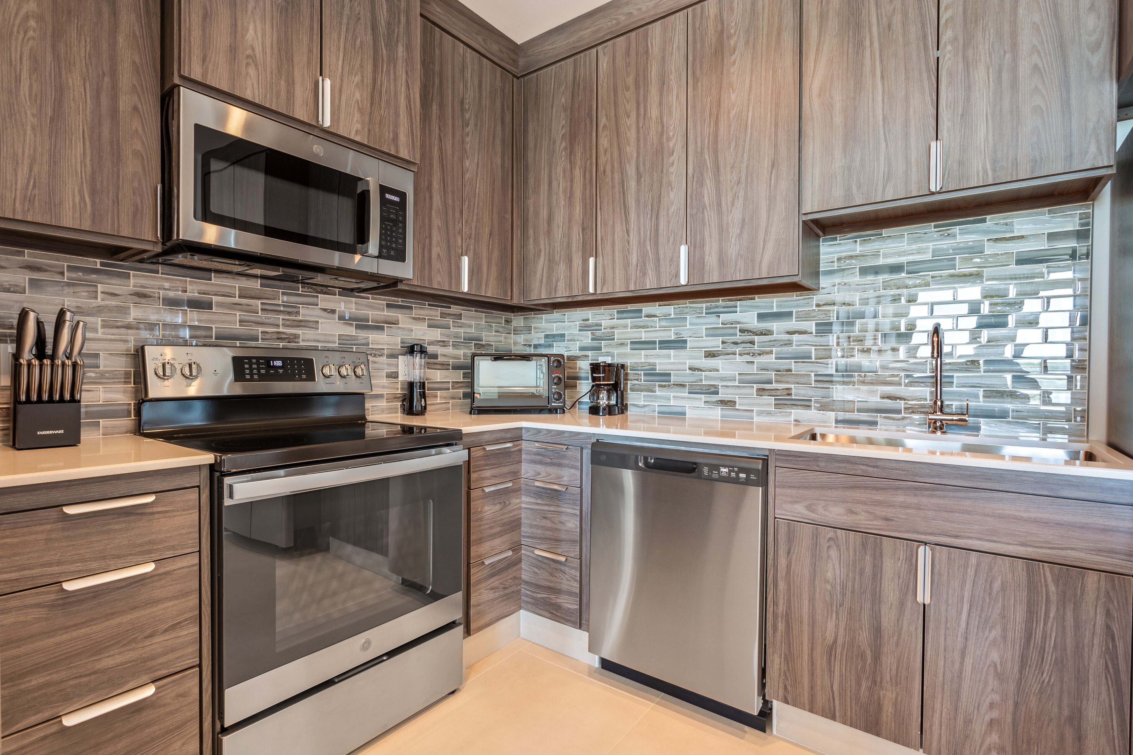 A modern kitchen with stainless steel appliances, wooden cabinets, and a tiled backsplash.