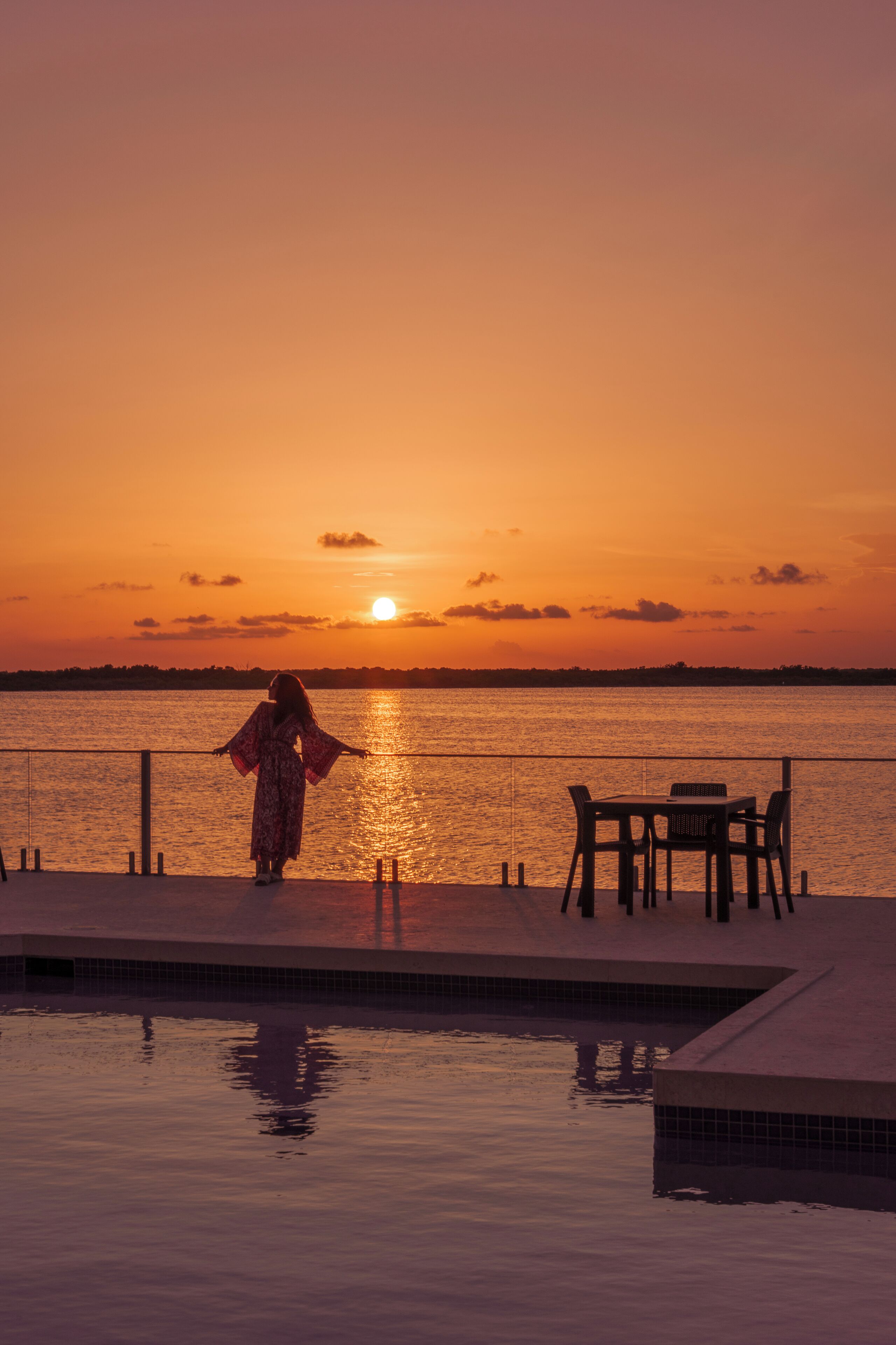 A person standing by a pool with a sunset view.