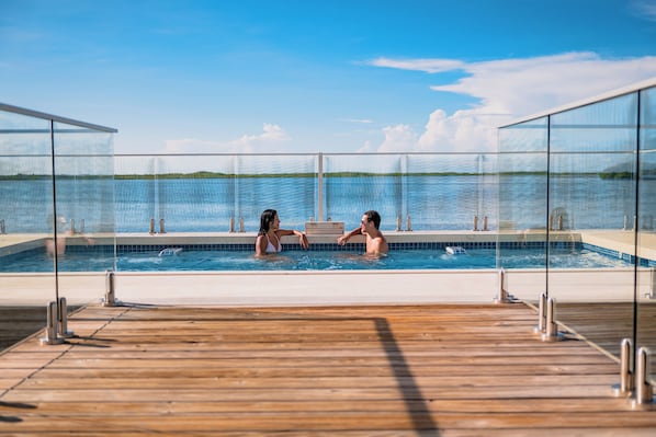 An outdoor swimming pool with glass railings, wooden deck, and a view of the water. - Sunset Caribe Belize (San Pedro)