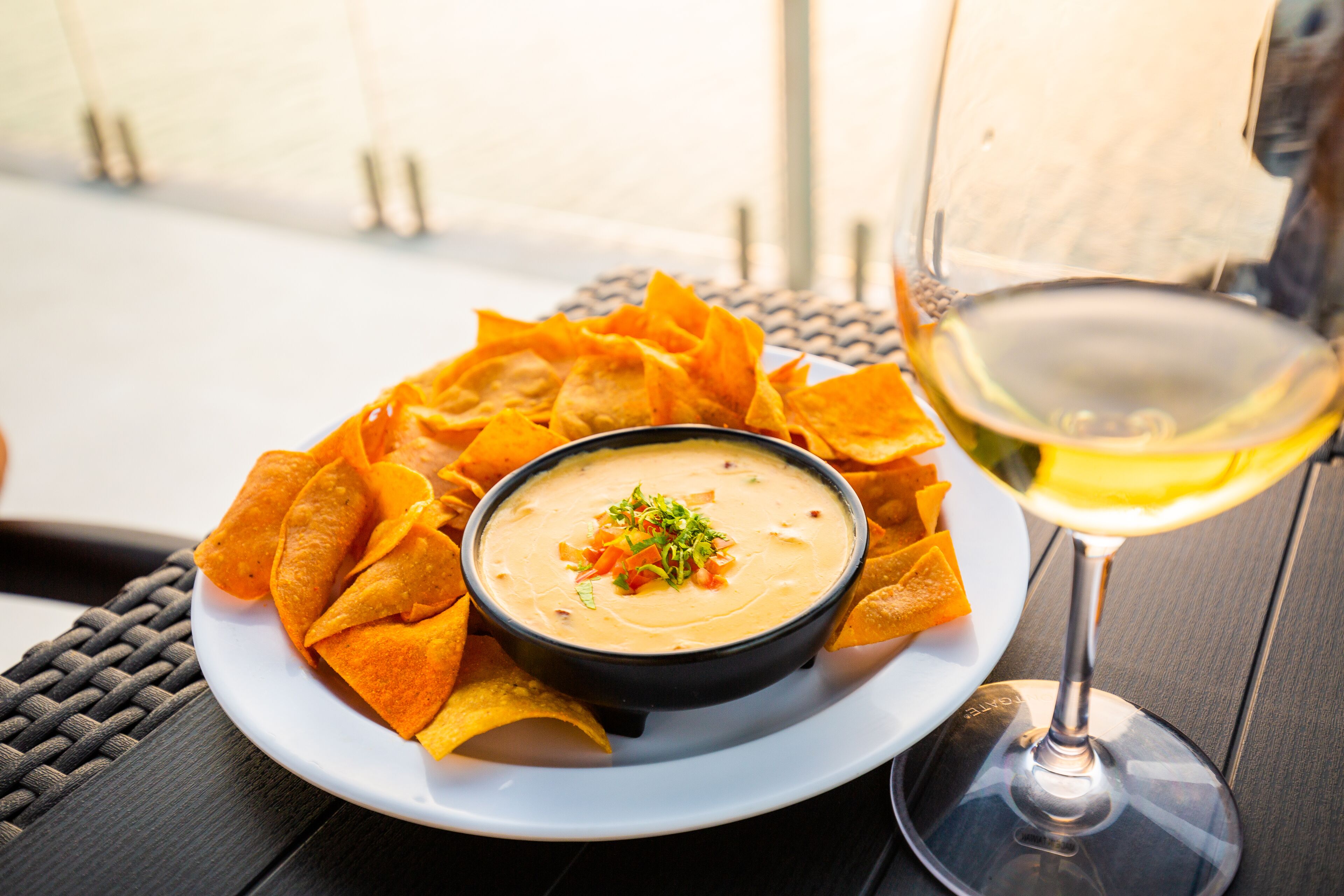 Un tazón de salsa cremosa con totopos sobre un plato, acompañado de una copa de vino blanco.