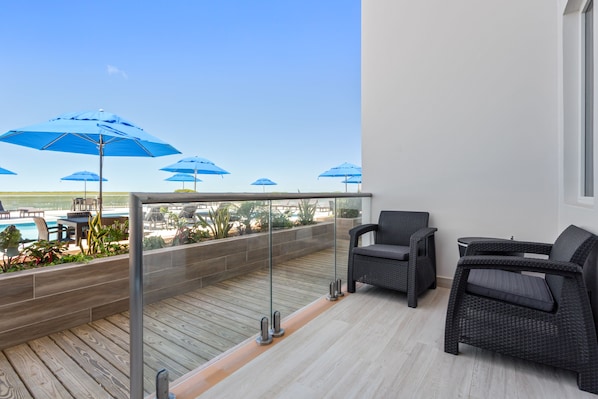 Un balcón con mobiliario de mimbre, sombrillas azules y vistas a una piscina y follaje.
