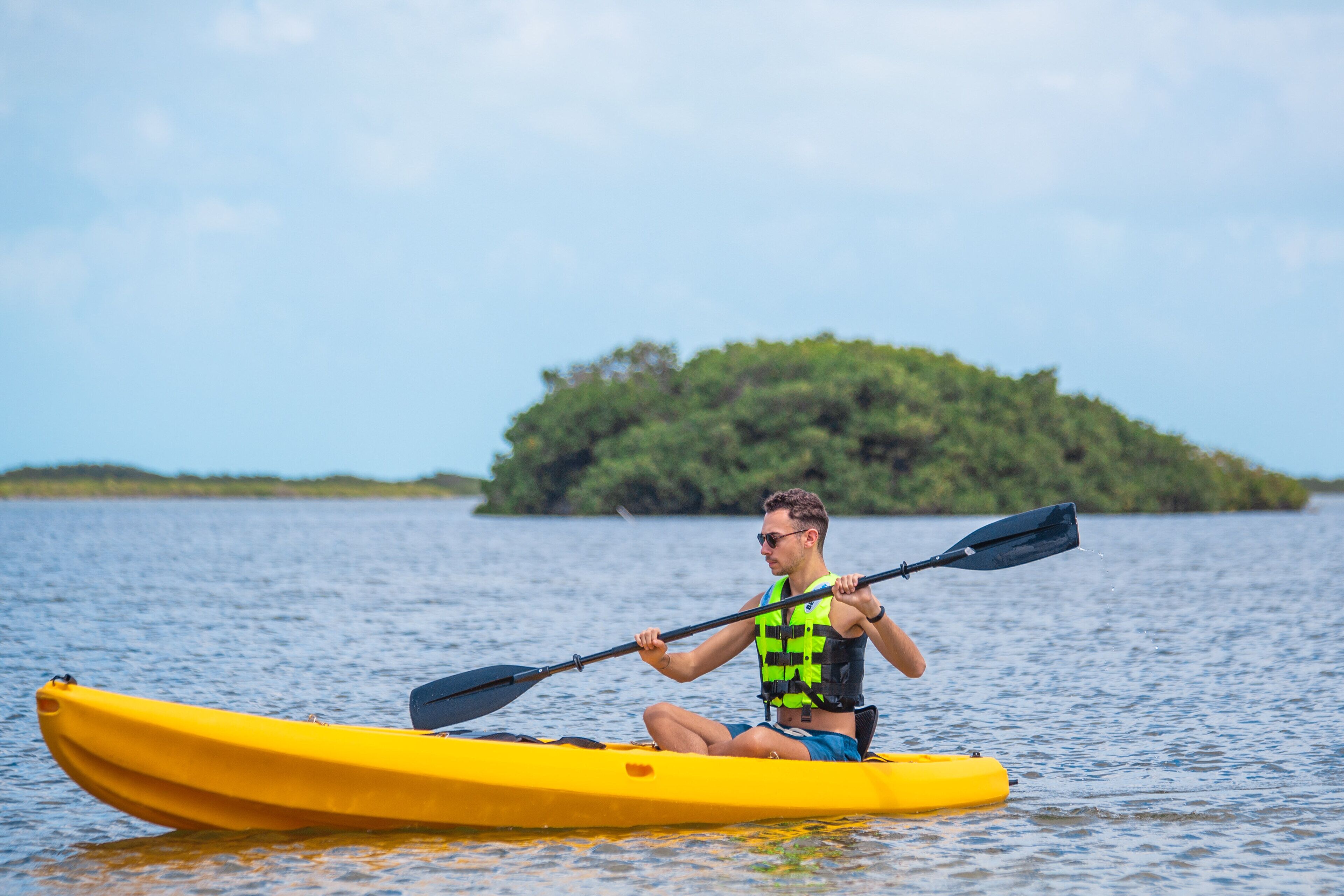 Una persona haciendo kayak en aguas tranquilas, con una pequeña isla al fondo.