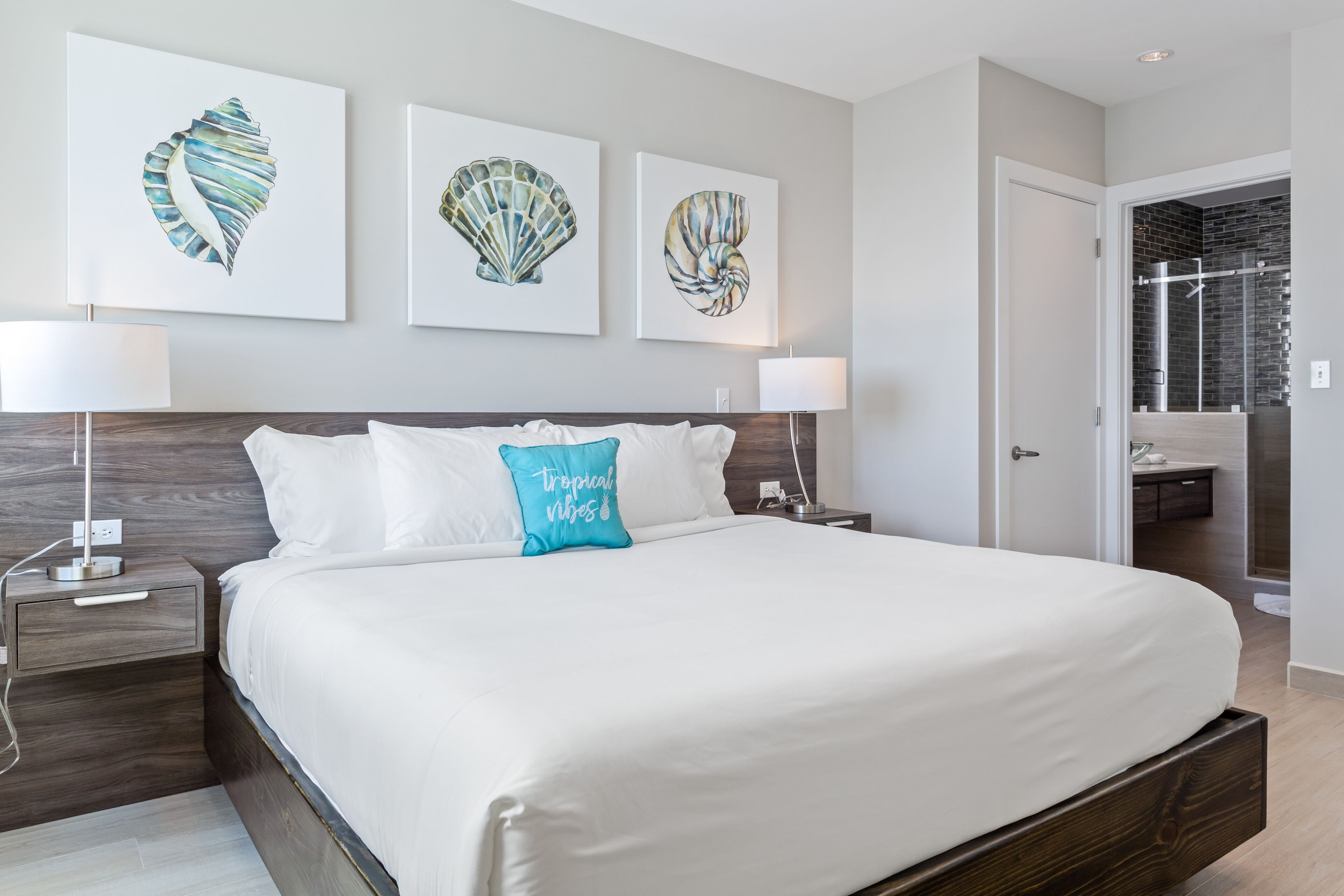 A modern hotel room with a large bed, two bedside tables, and three wall-mounted artworks.