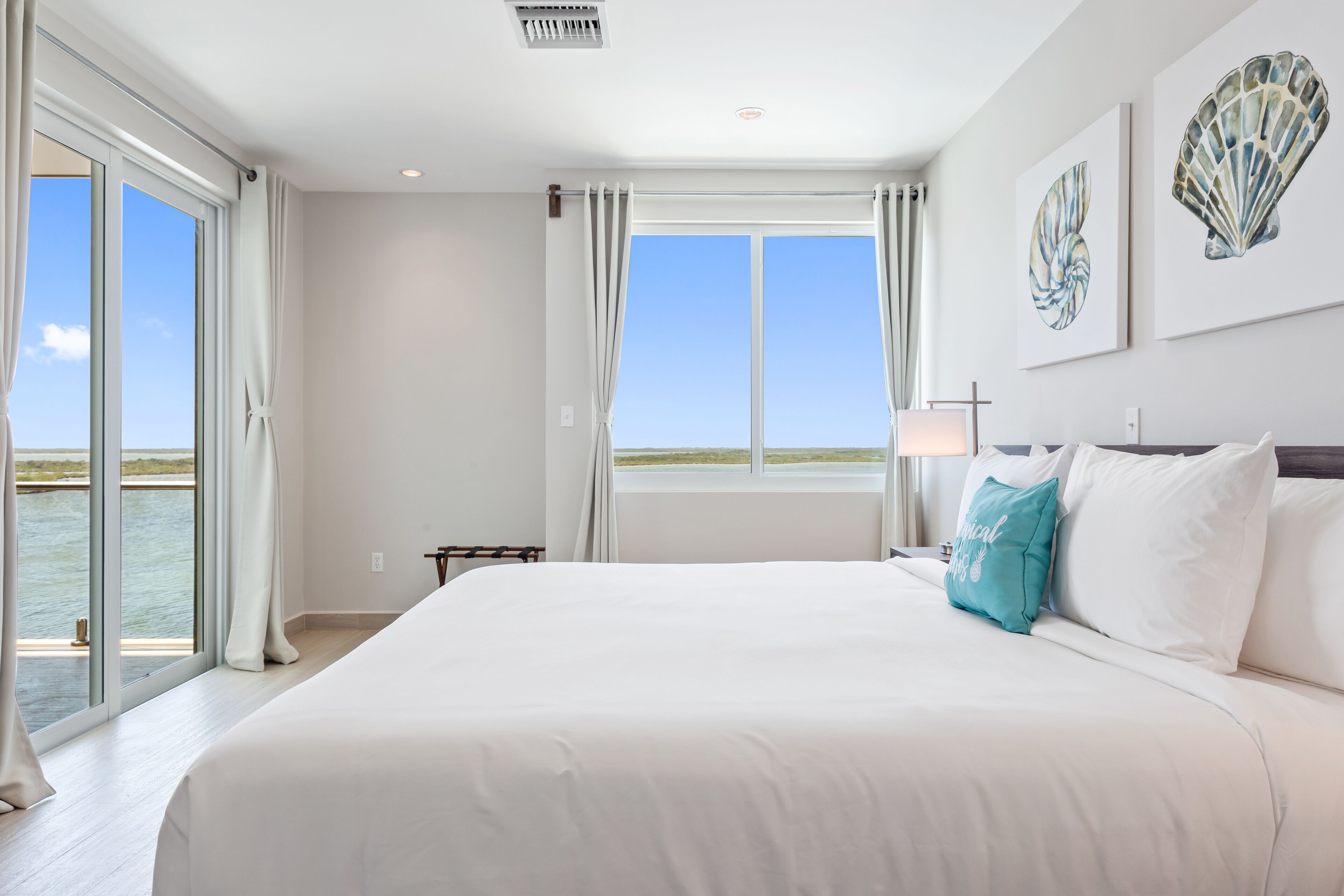 Un dormitorio espacioso con una cama grande, vistas al agua a través de las ventanas y un ventilador de techo.