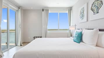 A spacious bedroom with a large bed, a view of the water through the windows, and a ceiling fan.