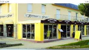 A yellow building with multiple storefronts, including 'L'ARTISAN DU PAI', 'SANDWICHERIE SNACKING', and 'PATISSERIE PAI'. - Apartment sables d'or les pins (Fréhel)