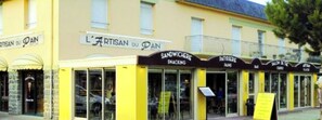 Un bâtiment jaune doté de nombreuses vitrines, parmi lesquelles on peut citer « L’ARTISAN DU PAI », « SANDWICHERIE SNACKING » et « PATISSERIE PAI ».