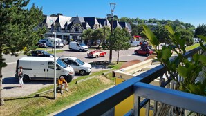 A parking lot with various vehicles, a building with a Tudor-style facade, and a clear blue sky. - Apartment sables d'or les pins (Fréhel)