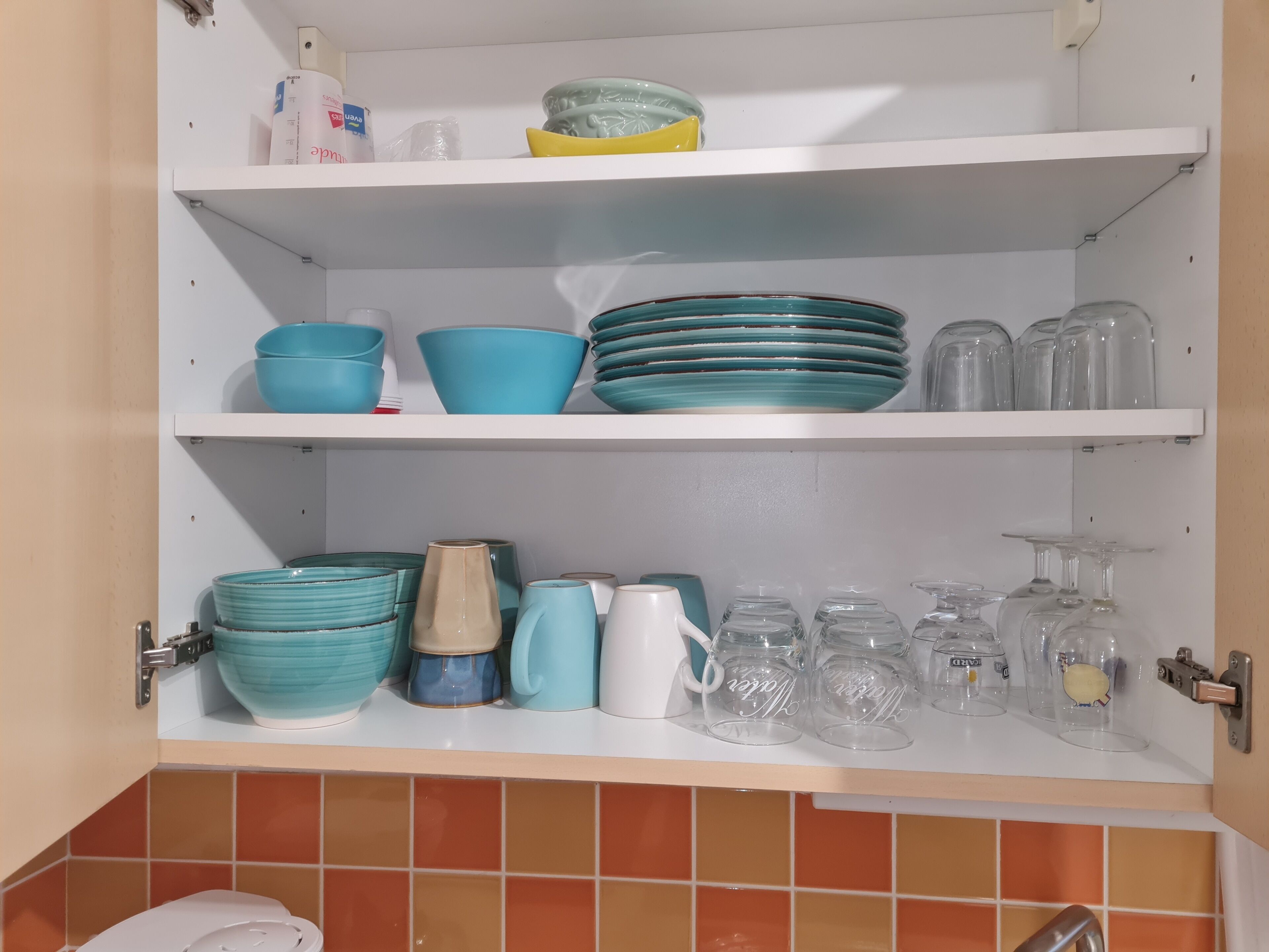 A kitchen with white shelves holding various dishes, cups, and glassware.
