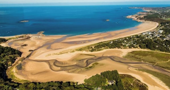 Vue aérienne d’une zone côtière avec une plage, des dunes de sable et des immeubles résidentiels.