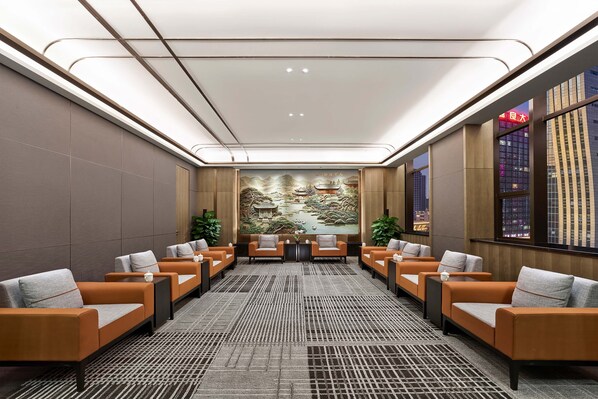 A modern hotel lobby with a seating area, a large mural, and a view of the cityscape through large windows. - Hilton Jiaxing (Jiaxing)