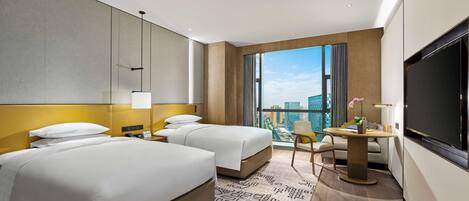 Habitación de hotel con dos camas, un escritorio con silla, un ventanal grande con vista a la ciudad y un televisor de pantalla plana.