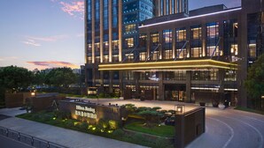 A modern hotel entrance with a well-lit facade, a landscaped garden area, and a sign indicating the hotel's name. - Hilton Jiaxing (Jiaxing)