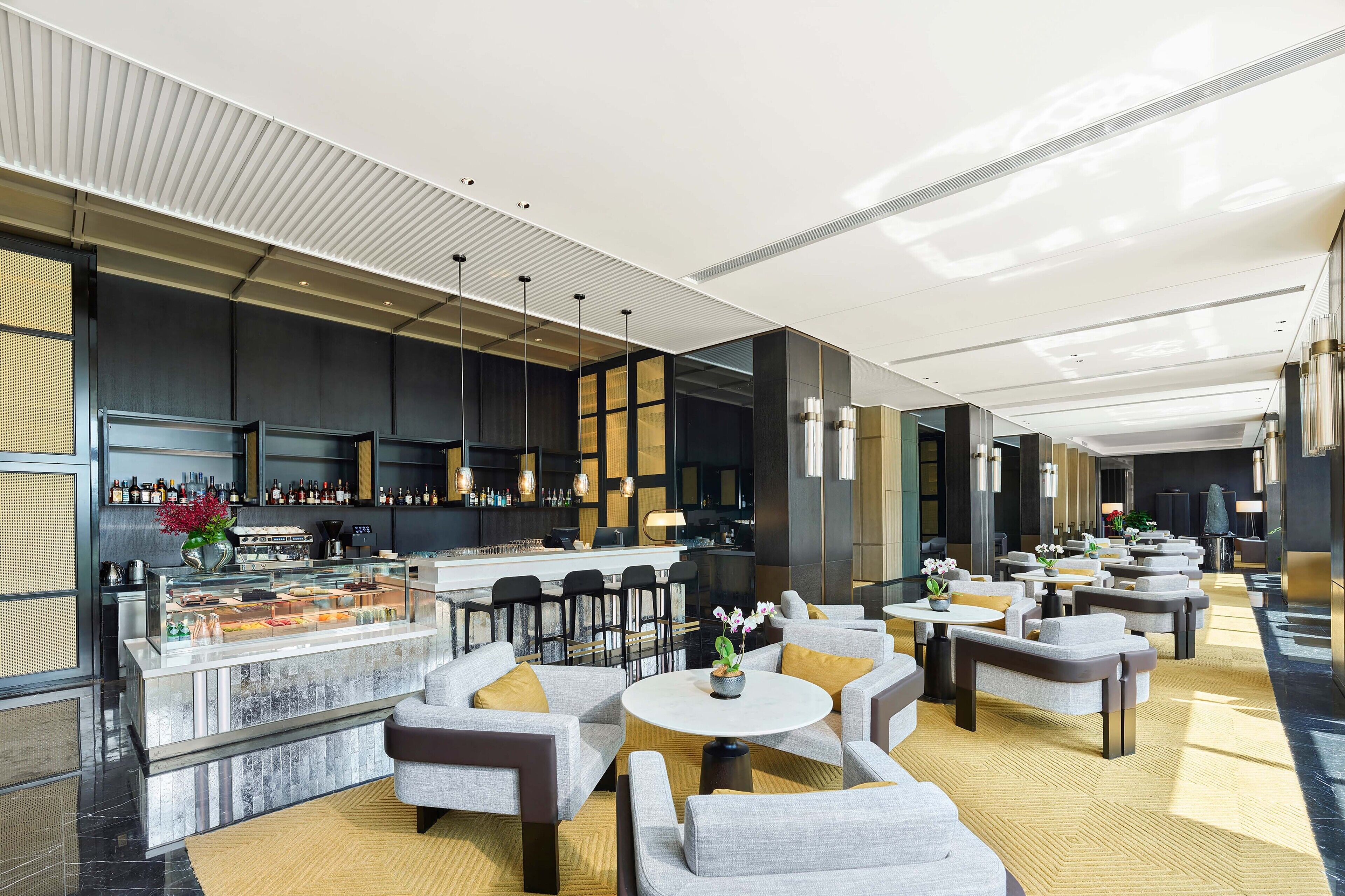 A modern hotel lobby with a bar area, seating arrangements, and a decorative centerpiece.