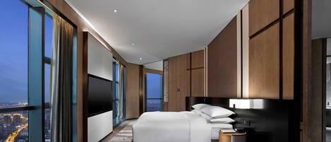 A modern bedroom with a large bed, a TV, and a view of a cityscape through large windows.