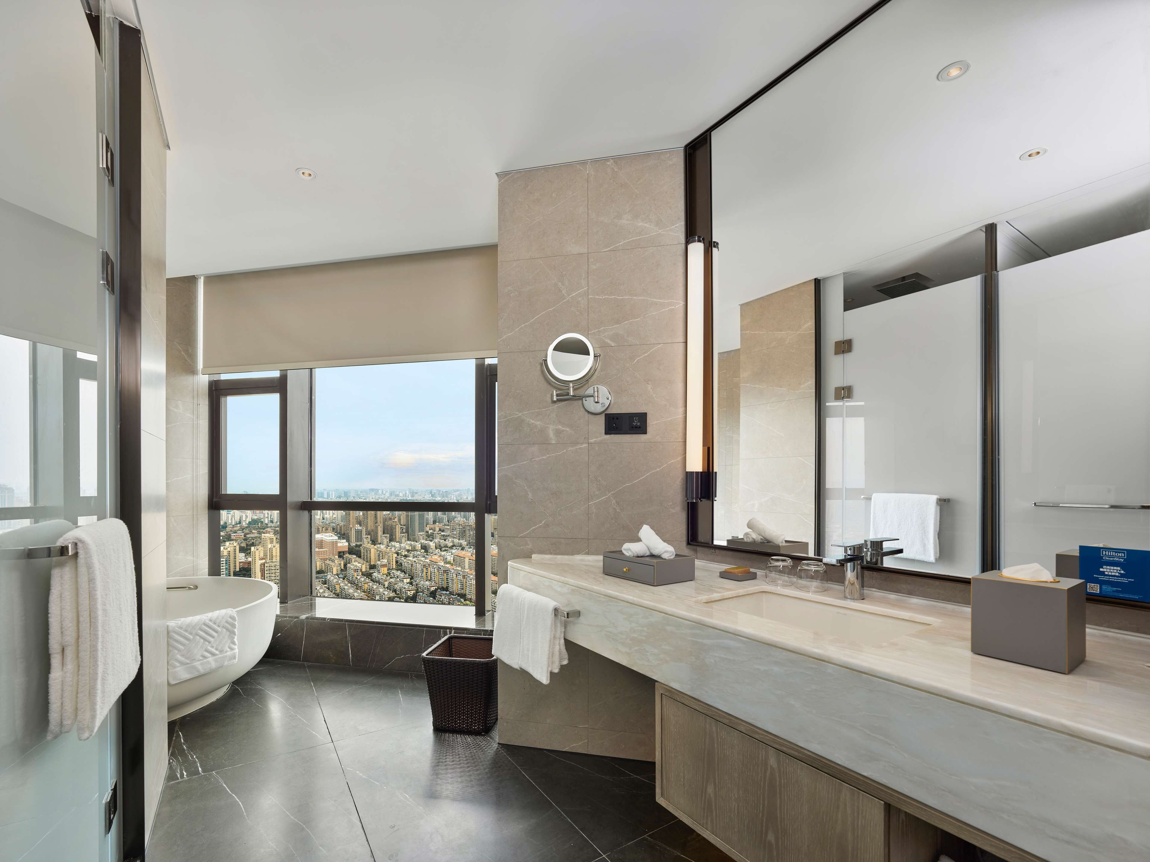 A modern bathroom with a large window, a bathtub, a vanity with a mirror, and a toilet.