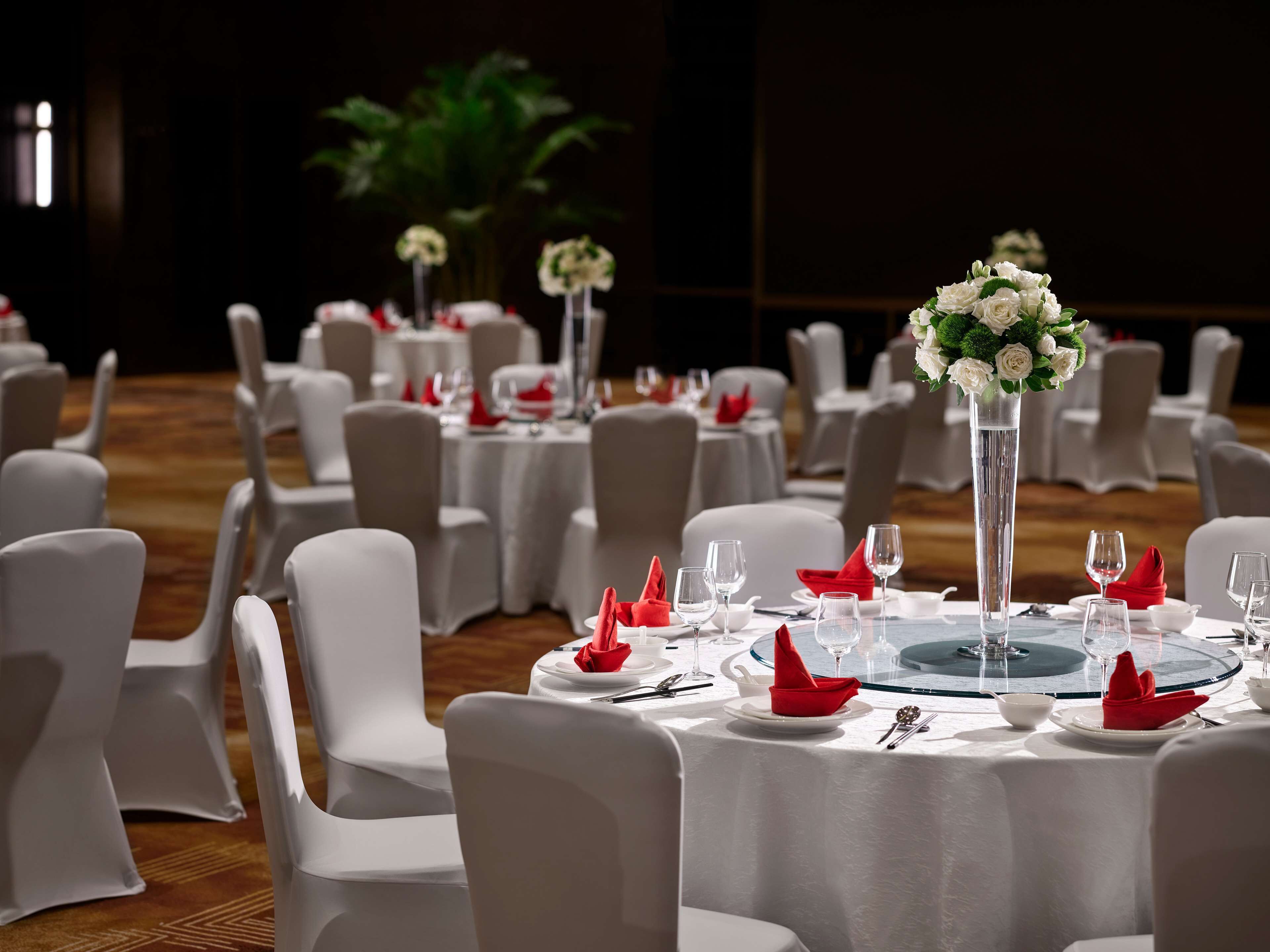 A banquet hall with round tables set for dining, white chairs, and red napkins.