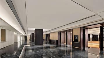 Um hall de hotel moderno com um corredor longo, pisos de mármore polido e uma combinação de madeira e painéis escuros nas paredes.