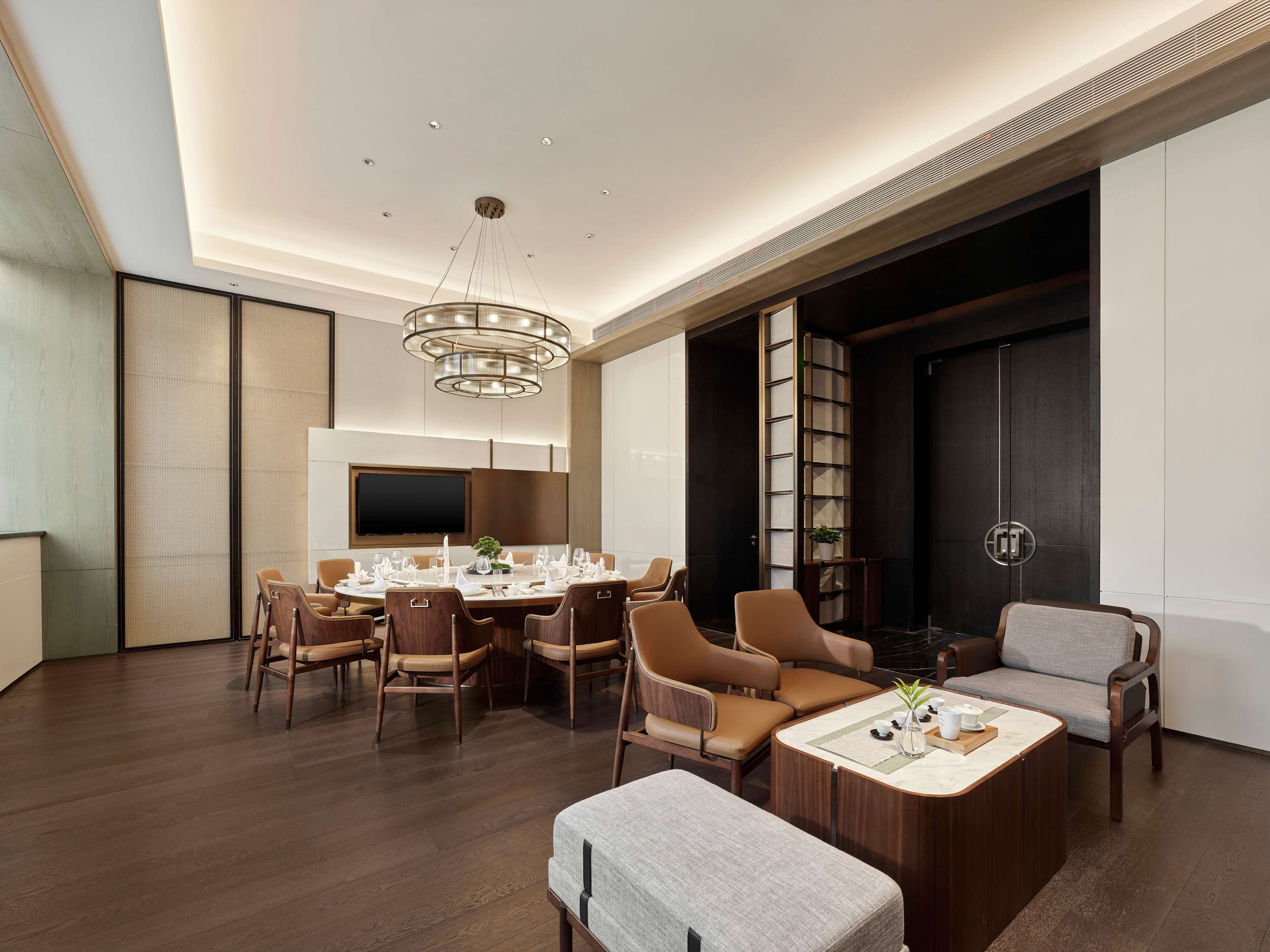 A modern dining area with a round table, multiple chairs, and a central chandelier.
