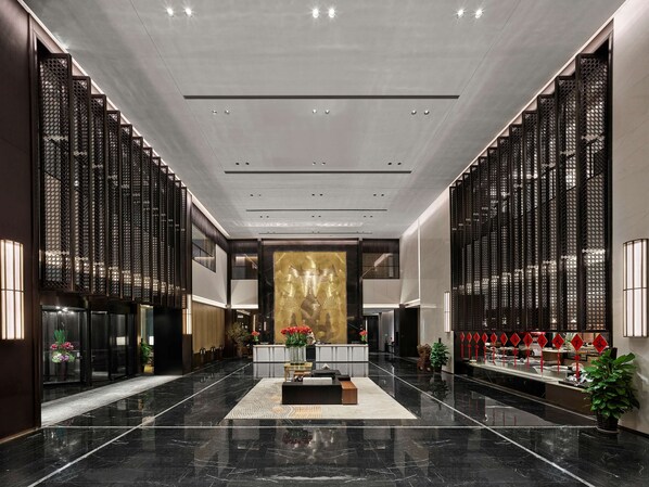 A spacious lobby with a polished marble floor, a reception desk, and decorative elements like plants and red signage.