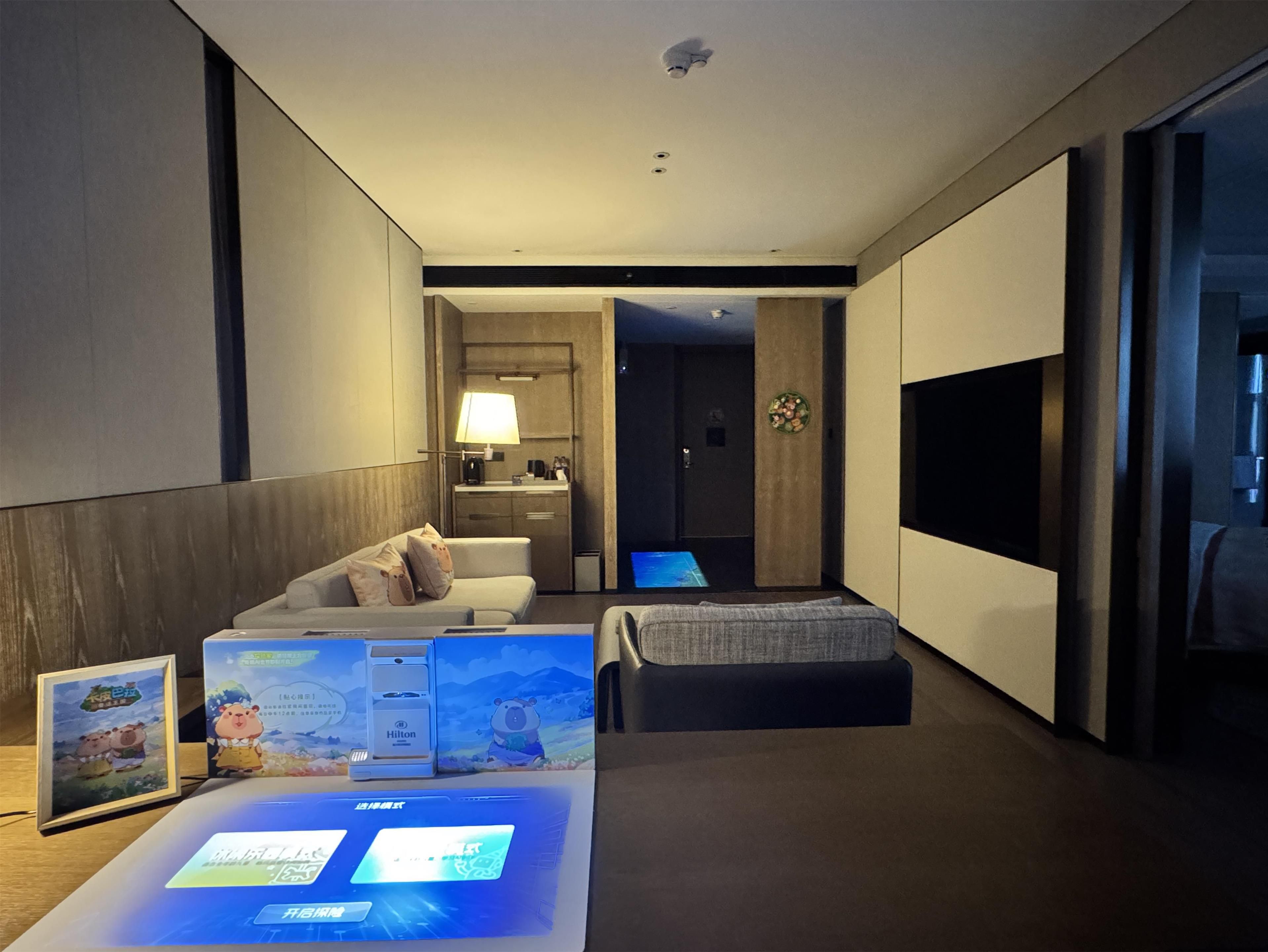 Ein modernes Hotelzimmer mit einer Couch, einem kleinen Bett, einem Schreibtisch mit einem Computer, einem Fernseher und einem sichtbaren Badezimmer im Hintergrund.