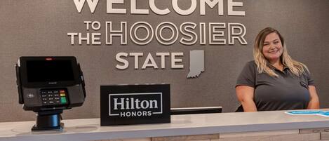 Un comptoir d’accueil avec une pancarte indiquant : « BIENVENUE DANS L’ÉTAT DE L’INDIANA » et « HILTON HONORS ».