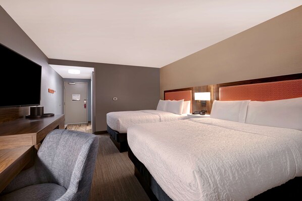 A hotel room with two beds, a desk, a chair, and a television.