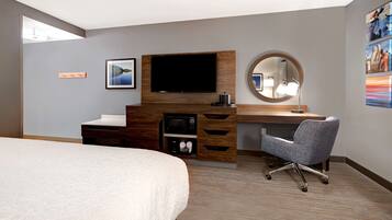 Habitación de hotel con cama, escritorio, televisor de pantalla plana, microondas y una silla.