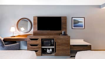 Une chambre d’hôtel avec un bureau en bois, un téléviseur à écran plat, un miroir, un tableau encadré et un lit.