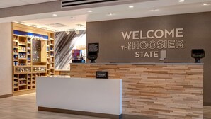 A hotel reception area with a 'Welcome to the Hoosier State' sign, a reception desk, and a shoe display.