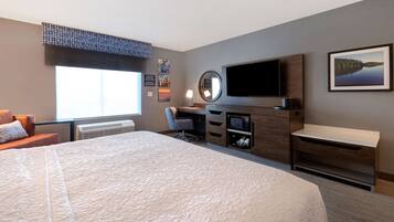 A hotel room with a large bed, a desk with a computer, a TV, and a window with blinds.