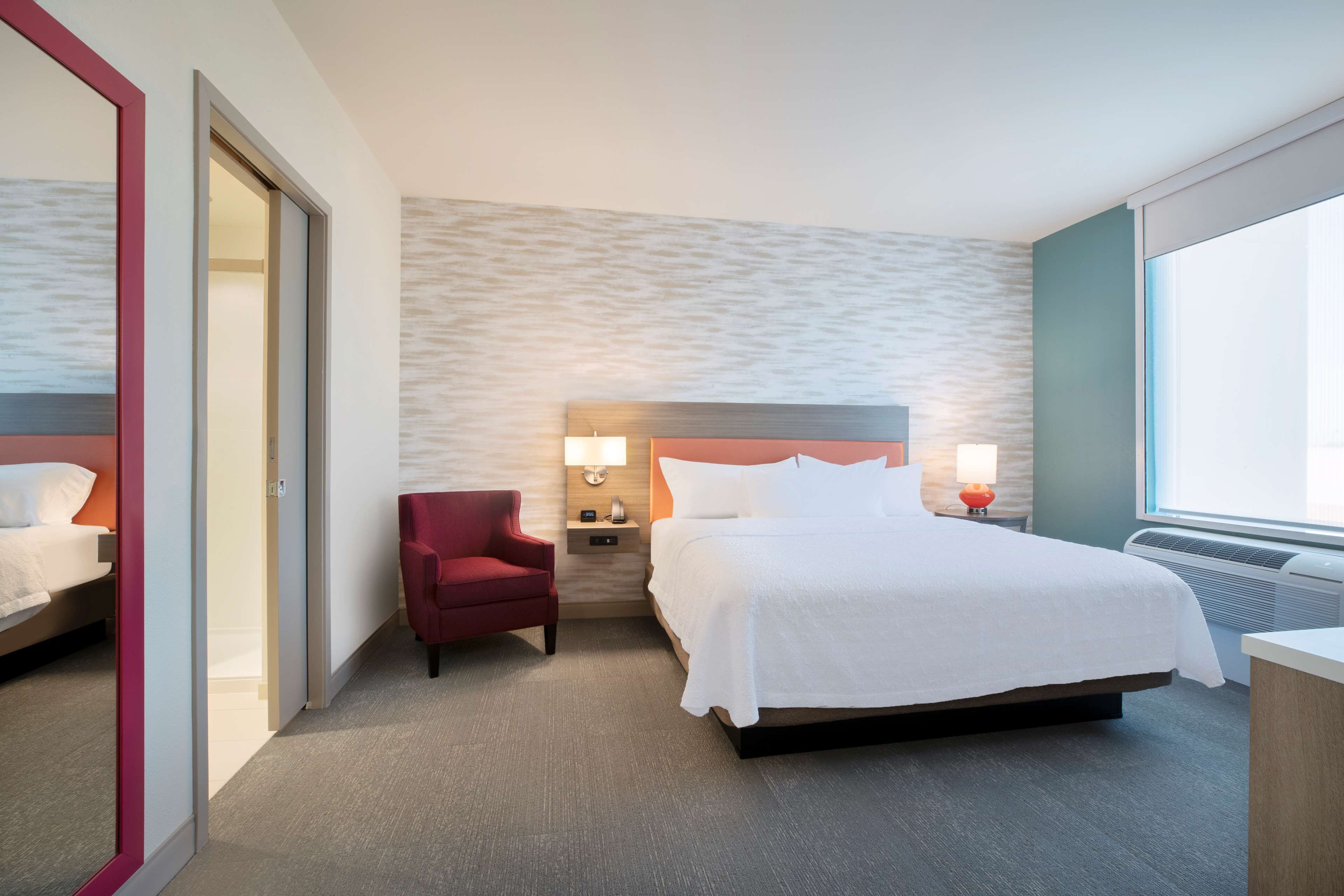 Une chambre d’hôtel avec un lit, une chaise, une table de chevet avec des lampes et une grande fenêtre.