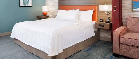 A hotel room with a bed, two bedside tables, a chair, and a wall with a textured pattern.