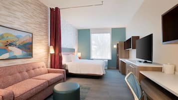 A modern hotel room with a bed, a sofa, a desk, a television, and a painting on the wall.