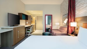 A hotel room with a bed, a desk, a TV, a chair, a sofa, a mirror, and a lamp. - Home2 Suites by Hilton Phoenix Avondale (Avondale)