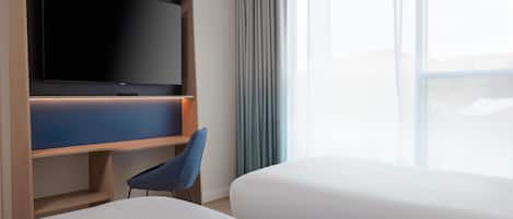 Habitación de hotel con un televisor de pantalla plana montado sobre un soporte de madera, una silla azul y dos camas.